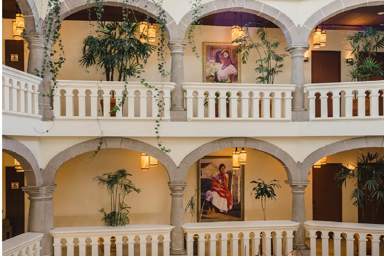 Corredores del patio de la Casona de los Sapos: dos pisos de arcos de cantera, plantas y pinturas de mujeres con vestido tradicional.