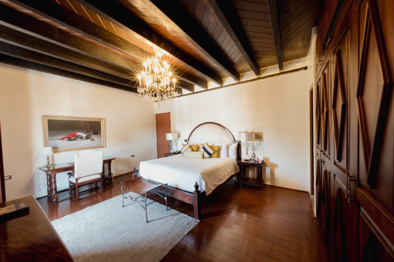 Suite de Lujo con cama king, techo de vigas de madera y candelabro.