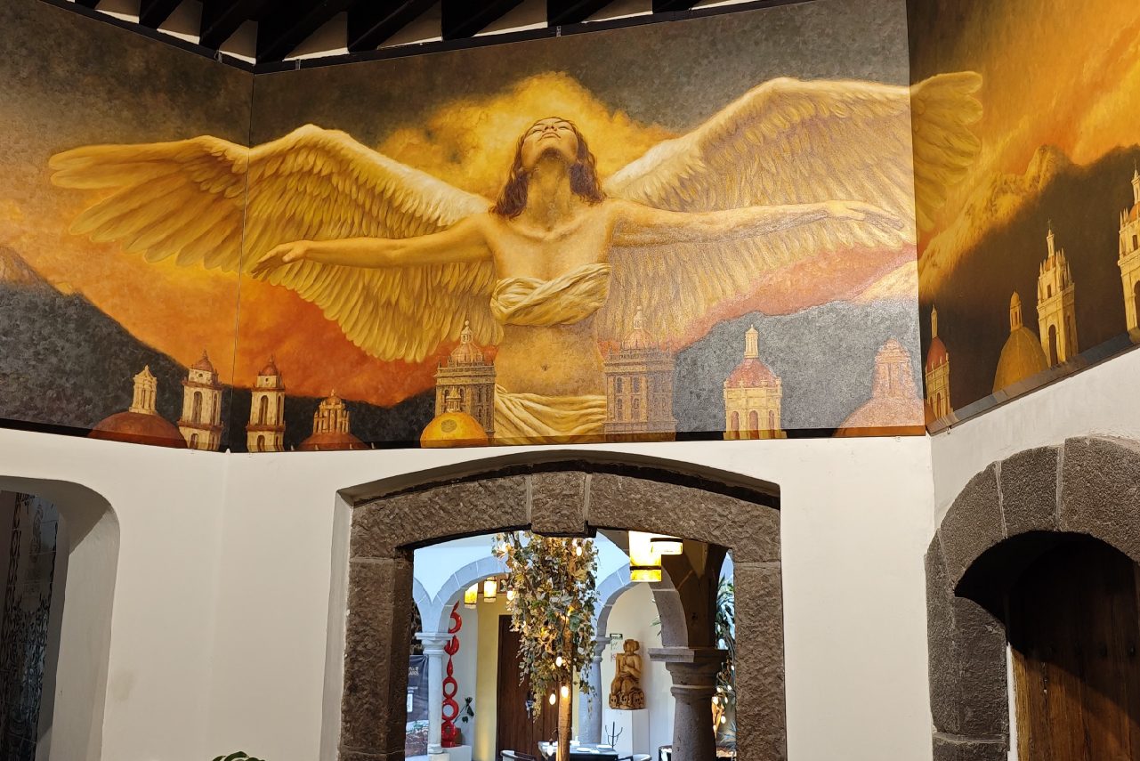 Mural de Fidel García en la Casona: un ángel con las alas abiertas sobre las cúpulas de Puebla.